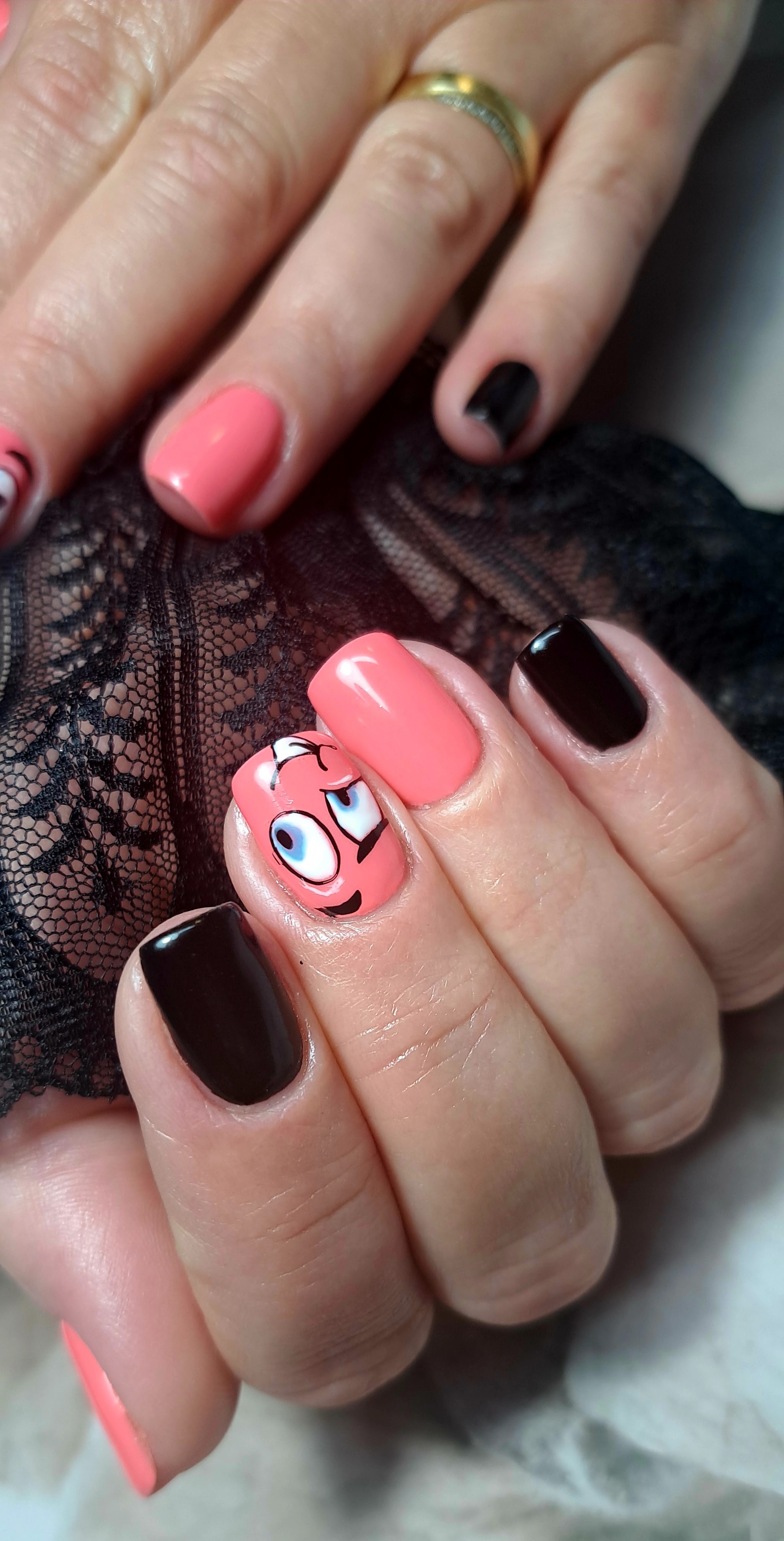 Koraalroze en zwarte nagels met een vrolijk getekend figuurtje
