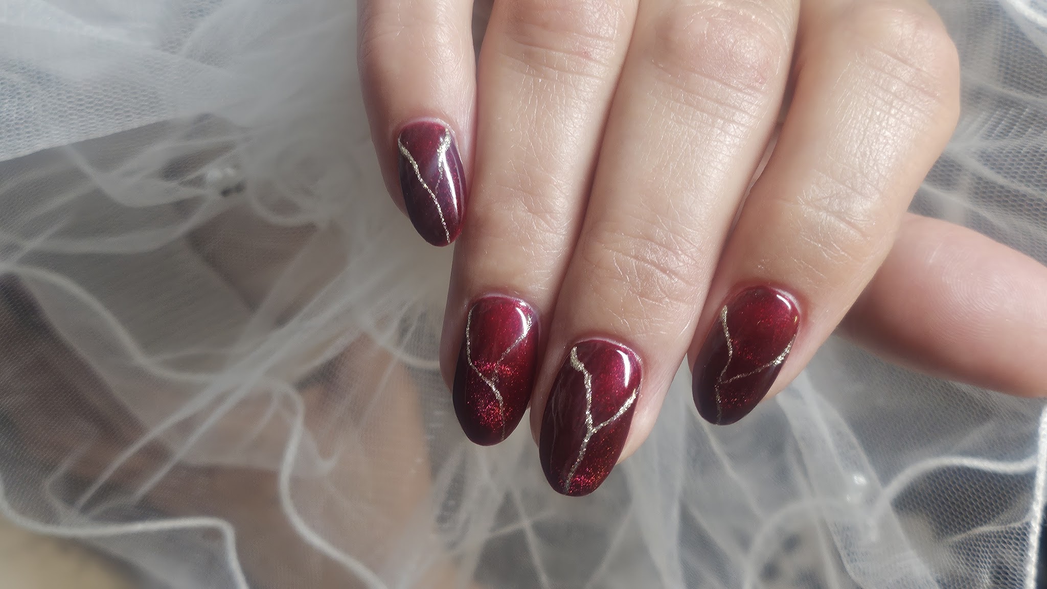 Wijnrode amandelnagels met dunne gouden adertjes, op tule